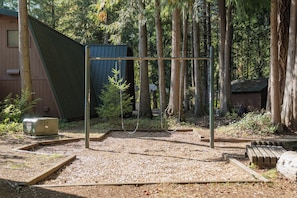Eine Holzterrasse mit einem Metall-Schaukelstuhl, umgeben von Bäumen und einem Gebäude mit einem geneigten Dach.