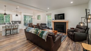A modern living room with a fireplace, leather recliner, and a kitchen area with bar stools.
