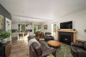 Una sala de estar moderna con chimenea, sofás de cuero, comedor y cocina con armarios blancos.