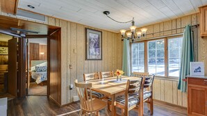 A wooden-paneled room with a dining table and chairs, a chandelier, and a window with curtains. - Lakefront Townsend Cabin w/ Fire Pit & Dock! (Townsend)