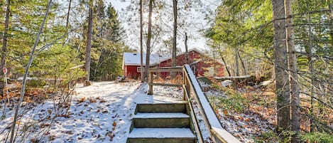 A wooden staircase leading to a red building surrounded by trees and snow-covered ground.