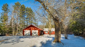 A red building with a garage, surrounded by trees and snow. - Lakefront Townsend Cabin w/ Fire Pit & Dock! (Townsend)