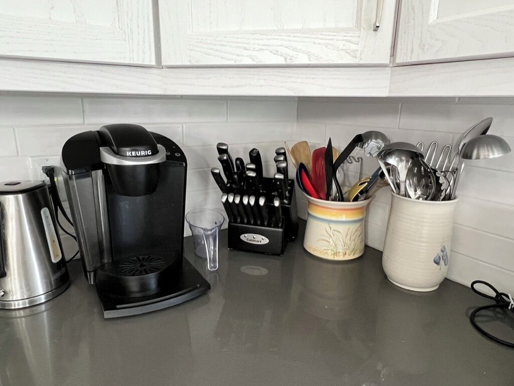 Una encimera de cocina con una cafetera Keurig, una jarra de café, un bloque de cuchillos, una taza con utensilios y un vaso.