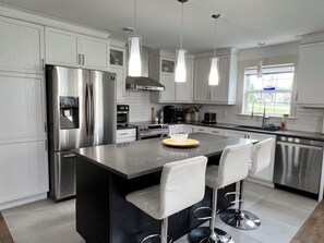 Een moderne keuken met roestvrijstalen apparatuur, witte kasten en een centraal eiland met barstoelen.