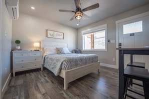 A bedroom with a bed, bedside table, lamp, ceiling fan, and a window.