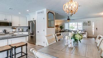 A spacious kitchen with white cabinetry, a central island with stools, a dining table with chairs, and a chandelier.