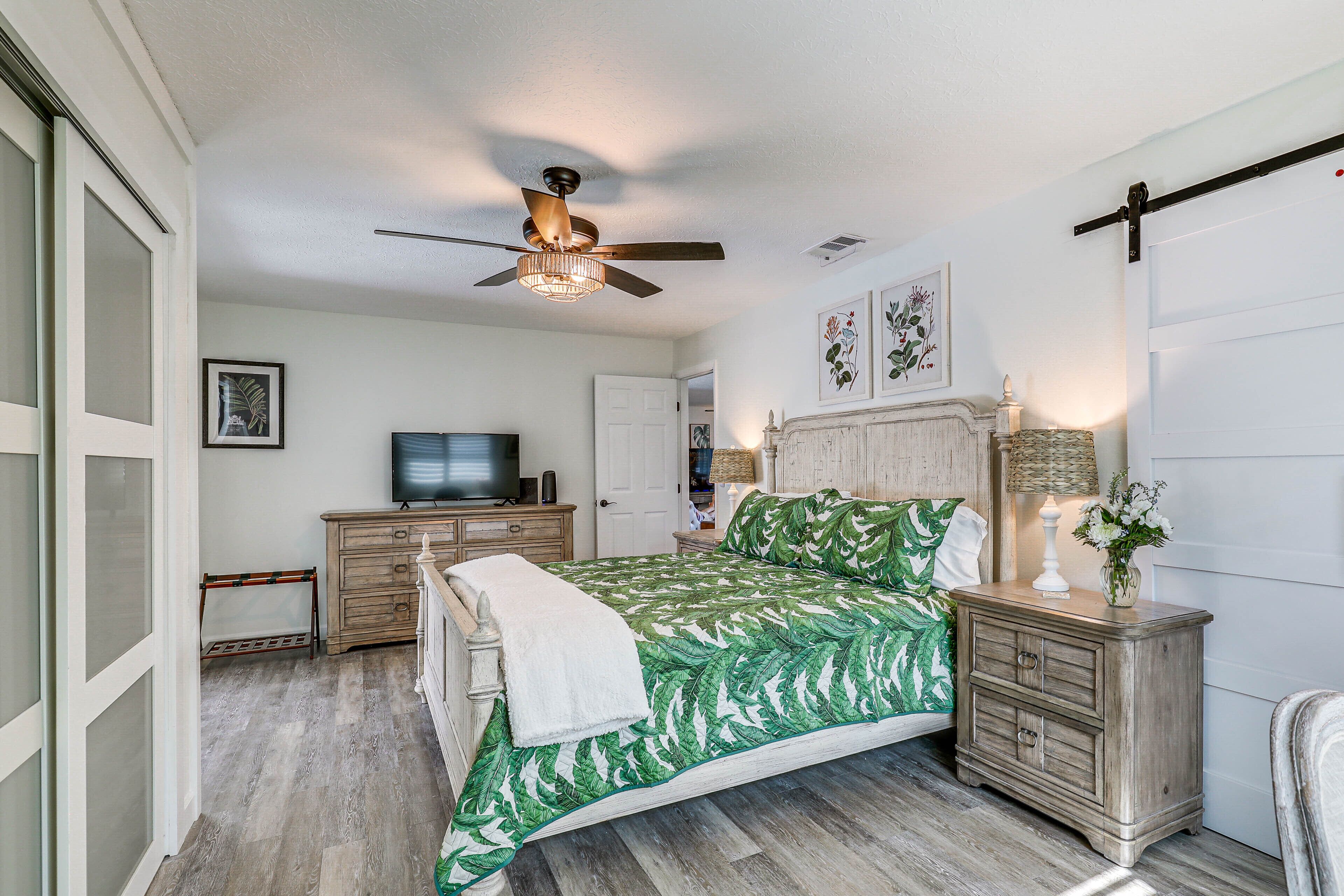A bedroom with a bed, a ceiling fan, a television, a nightstand, and a door.