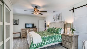 A bedroom with a bed, a ceiling fan, a television, a nightstand, and a door.
