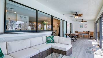 A spacious patio area with a white sofa, wicker furniture, ceiling fans, and a view of the kitchen.