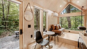 Una cabaña moderna con ventanas amplias, un espejo redondo, un sofá y un comedor.