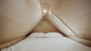 A triangular room with a bed, a skylight, and a ceiling light.