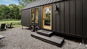 A small, modern cabin with a sliding door, a small porch, and a gravel driveway.