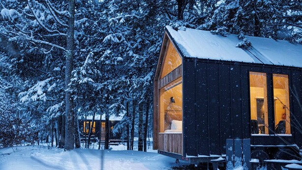 A cozy cabin with a large window, a fire pit, and a bench outside.