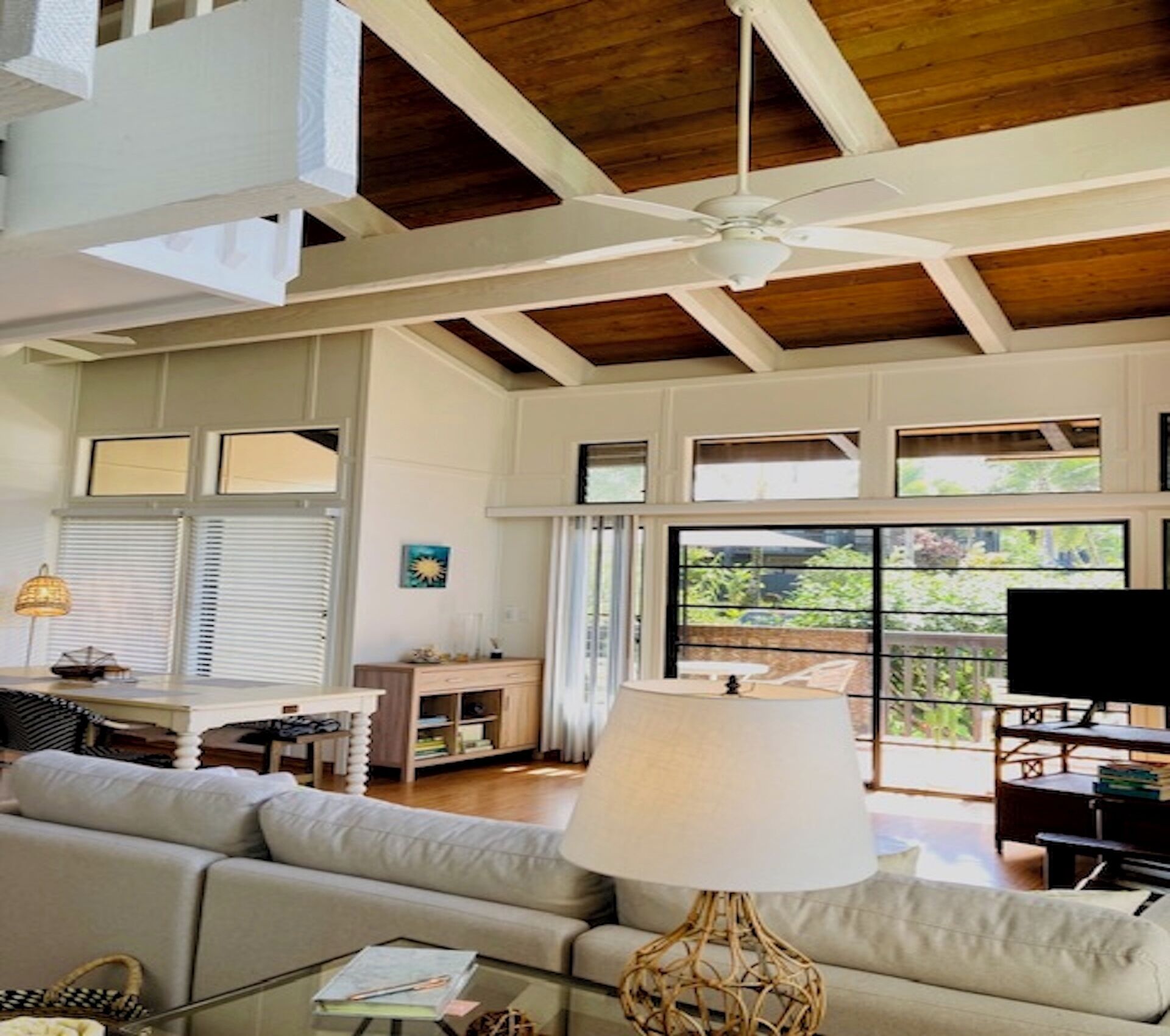 A spacious living room with a high ceiling, large windows, a ceiling fan, and a television.