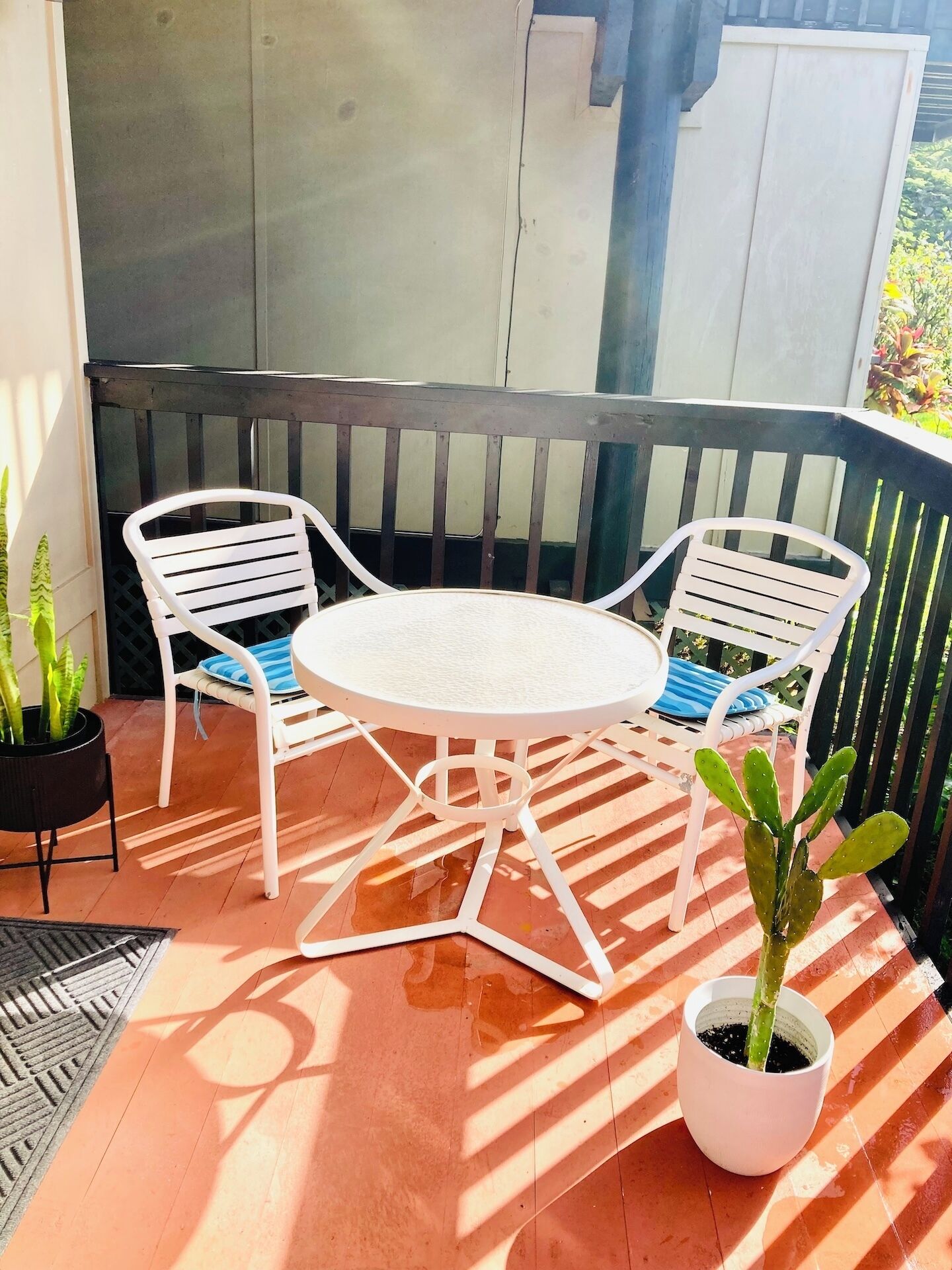 A patio with a round table and two white chairs, surrounded by potted plants.