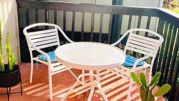 A patio with a round table and two white chairs, surrounded by potted plants.