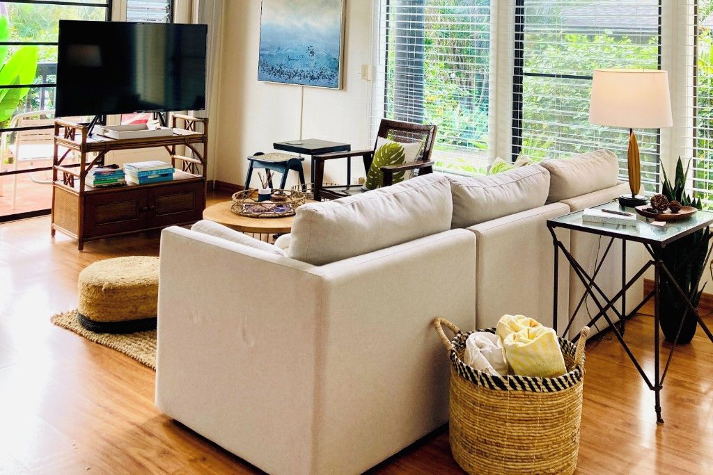Un salón con sofá, televisión sobre un mueble de madera, un cuadro en la pared y una ventana con persianas.
