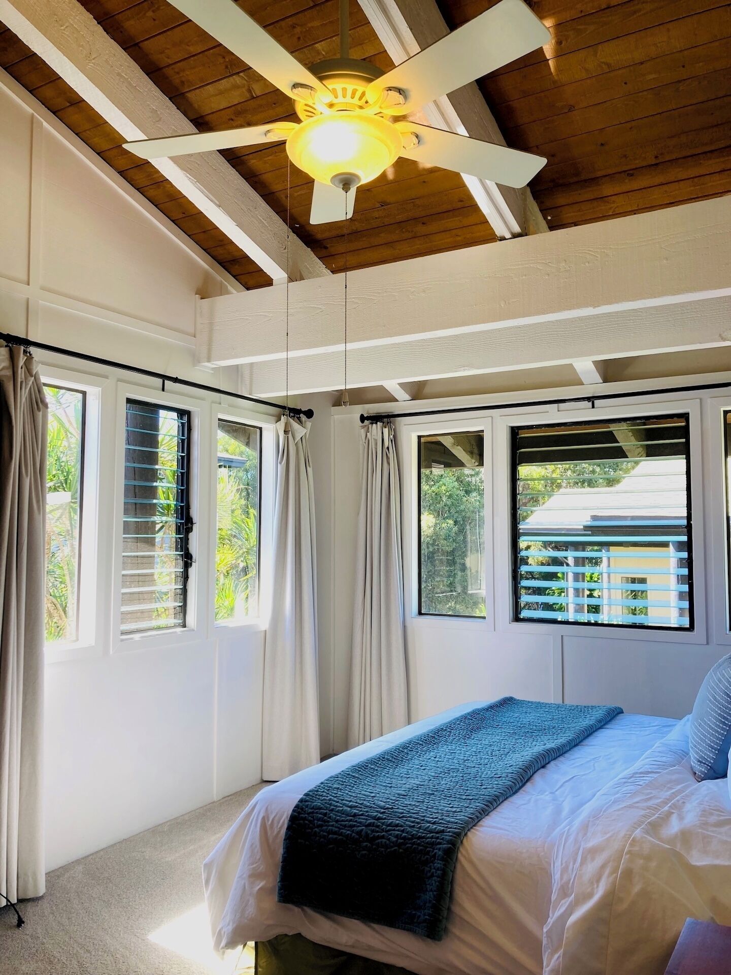A bedroom with a bed, a ceiling fan, and windows with curtains.
