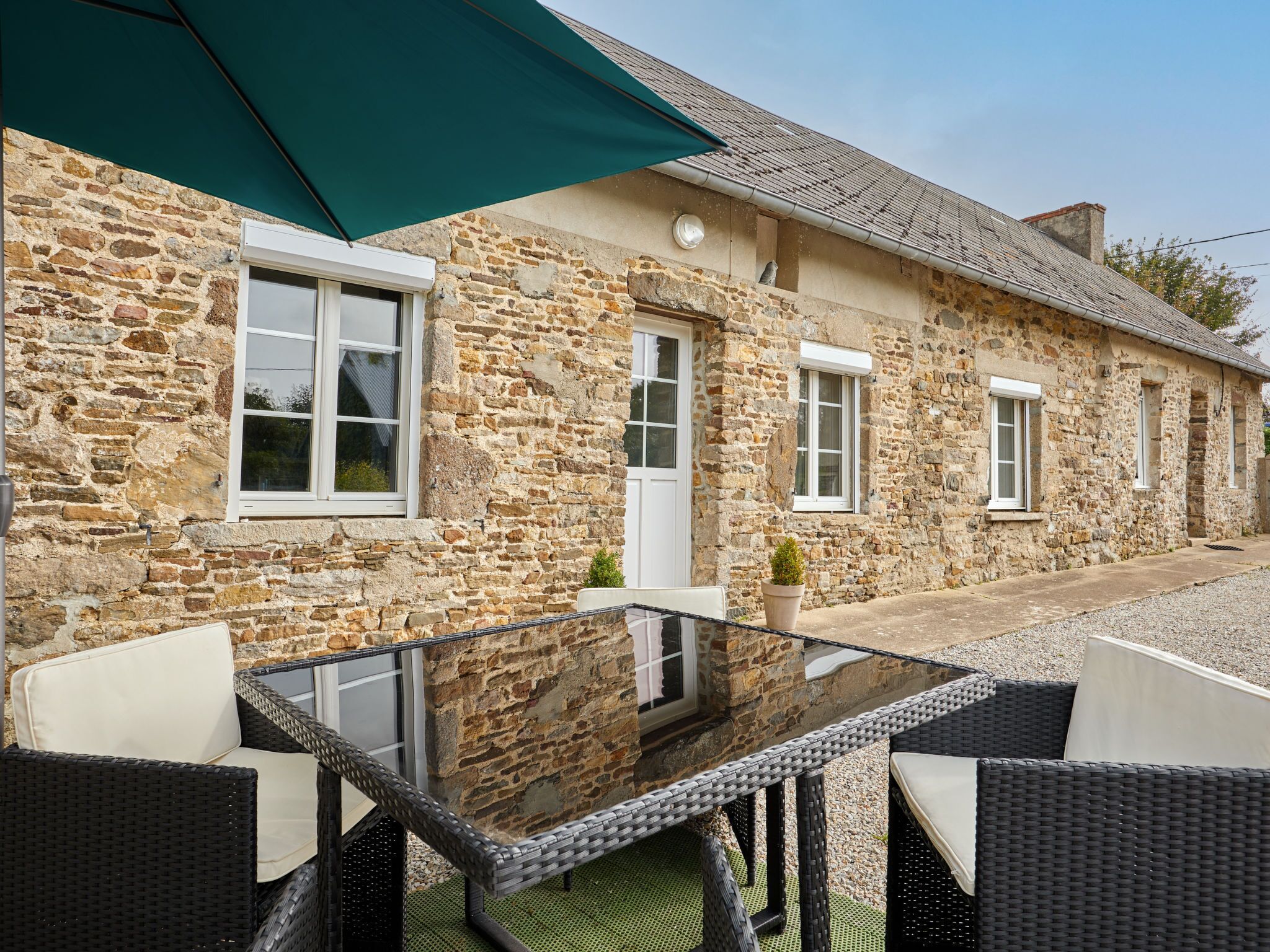 Un bâtiment en pierre avec une table en verre et des chaises en osier à l’extérieur.