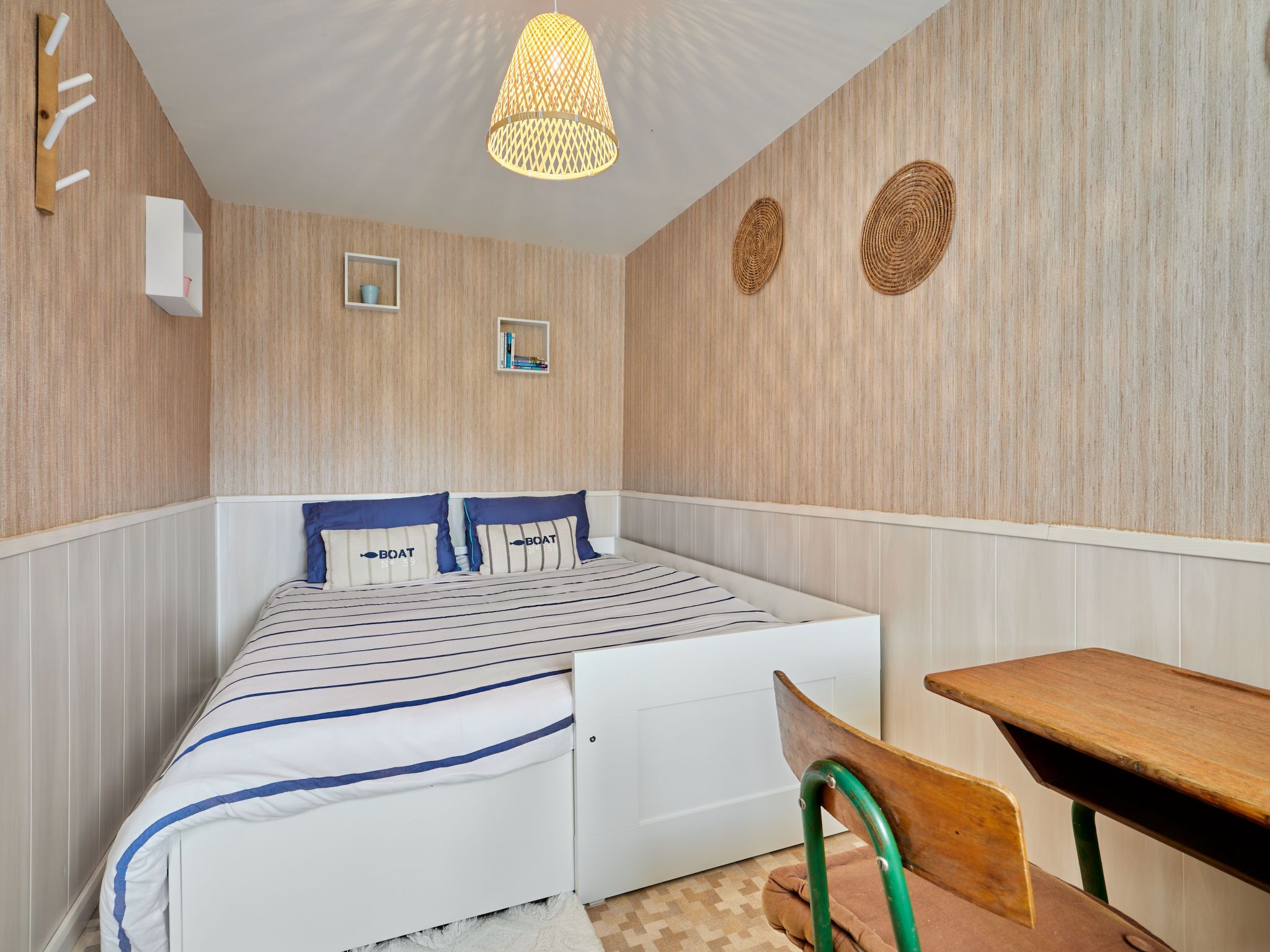 Een slaapkamer met een bed, een bureau en een stoel. Er zijn wandplanken en een hangende lamp.