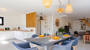 Une cuisine moderne avec des meubles blancs, un mur d’accent en bois et un coin repas comprenant une longue table et des chaises bleues.