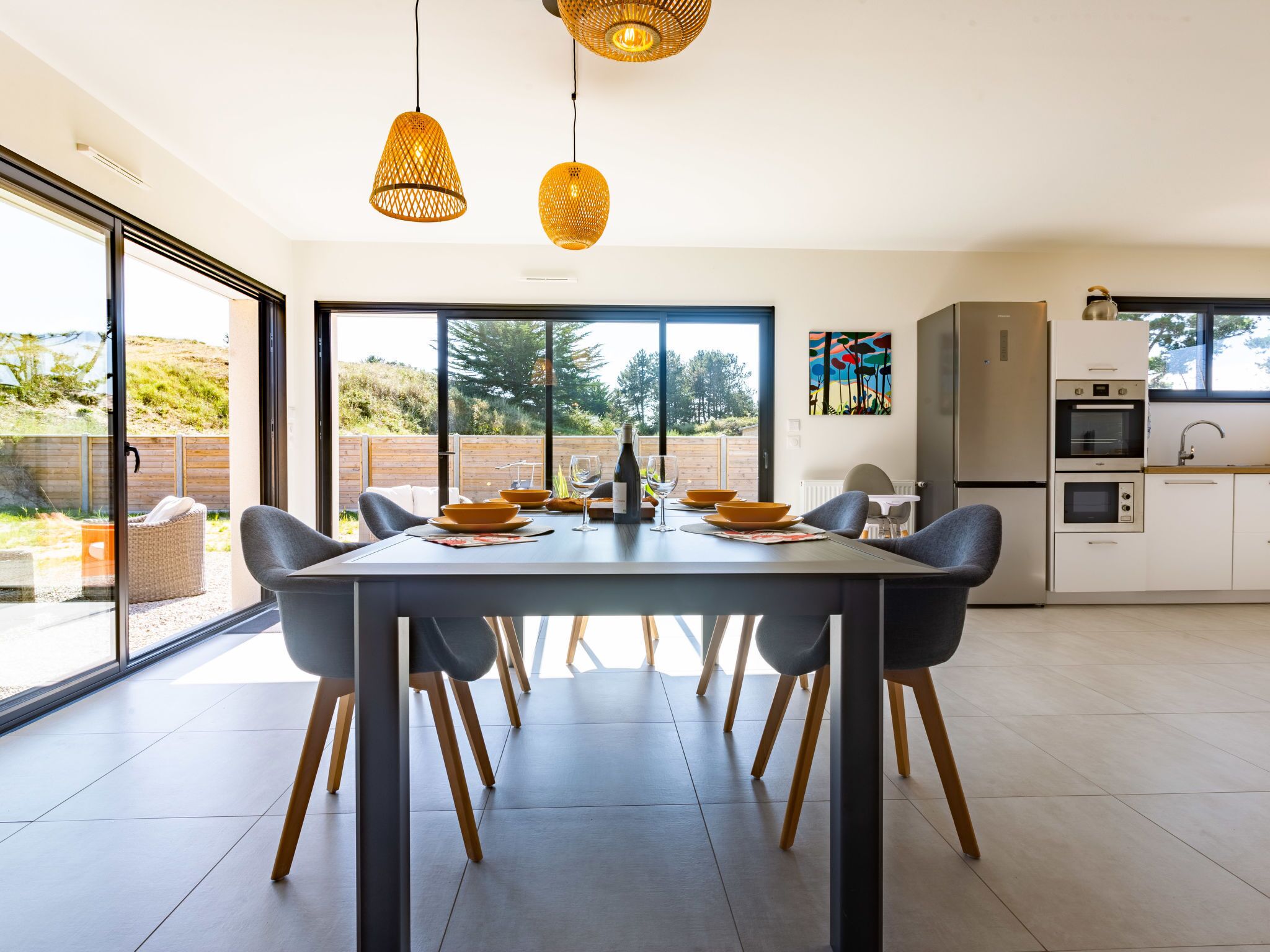 A modern kitchen with a dining area, large windows, and a view of the outdoors.