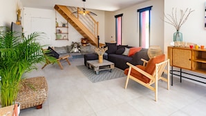 Un salon moderne avec un canapé, une table basse et une chaise en bois. Un escalier avec une rampe en bois mène à un niveau supérieur.