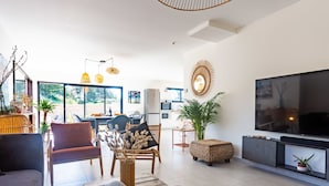 Un salon moderne doté d’un grand téléviseur, de sièges confortables et d’un coin repas baigné de lumière naturelle.