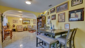 Un coin repas avec une table et des chaises en bois, un ventilateur de plafond et une bibliothèque contenant divers objets.