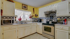 Une cuisine avec des meubles blancs, un four à micro-ondes, une cuisinière et un évier.