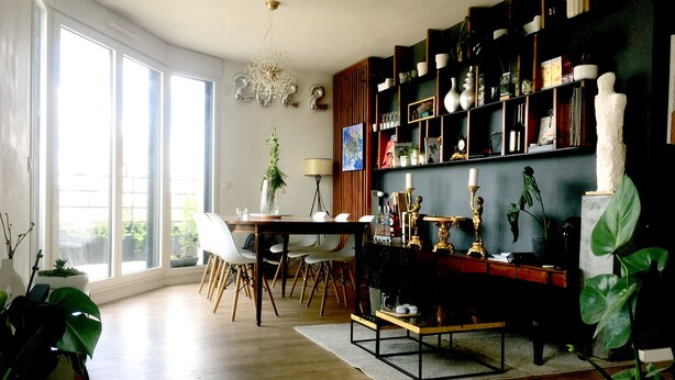 Un comedor moderno con un amplio ventanal, una mesa de comedor con sillas y una estantería llena de objetos varios.