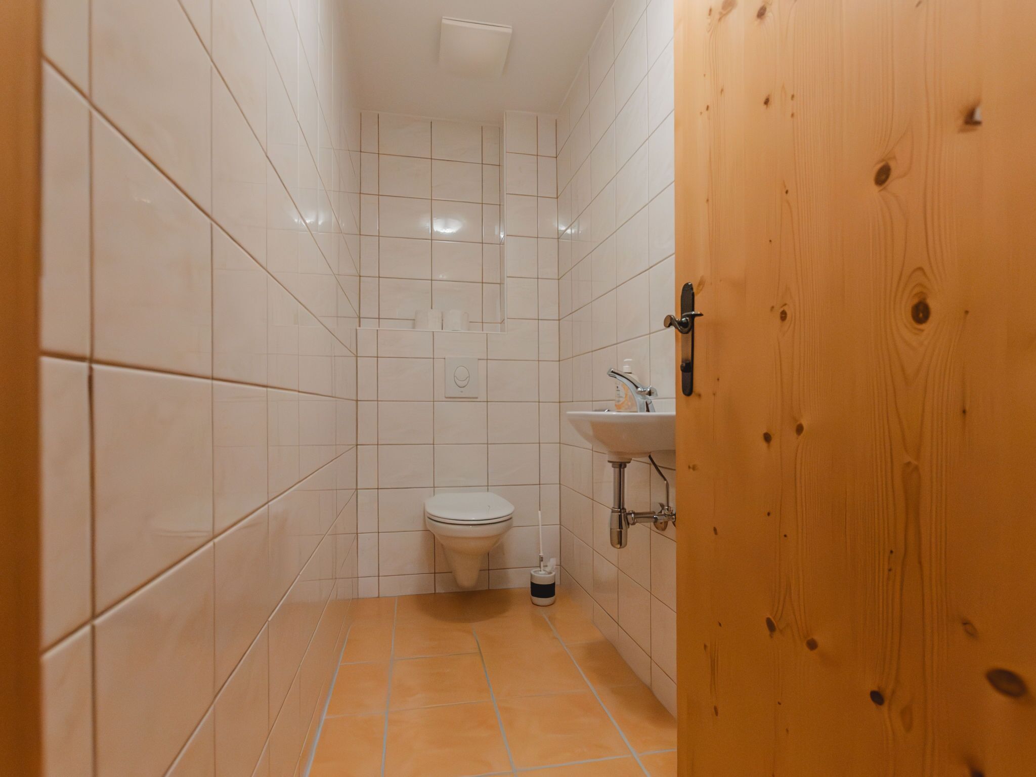 Een kleine badkamer met tegels, een toilet, een wastafel en een houten deur.