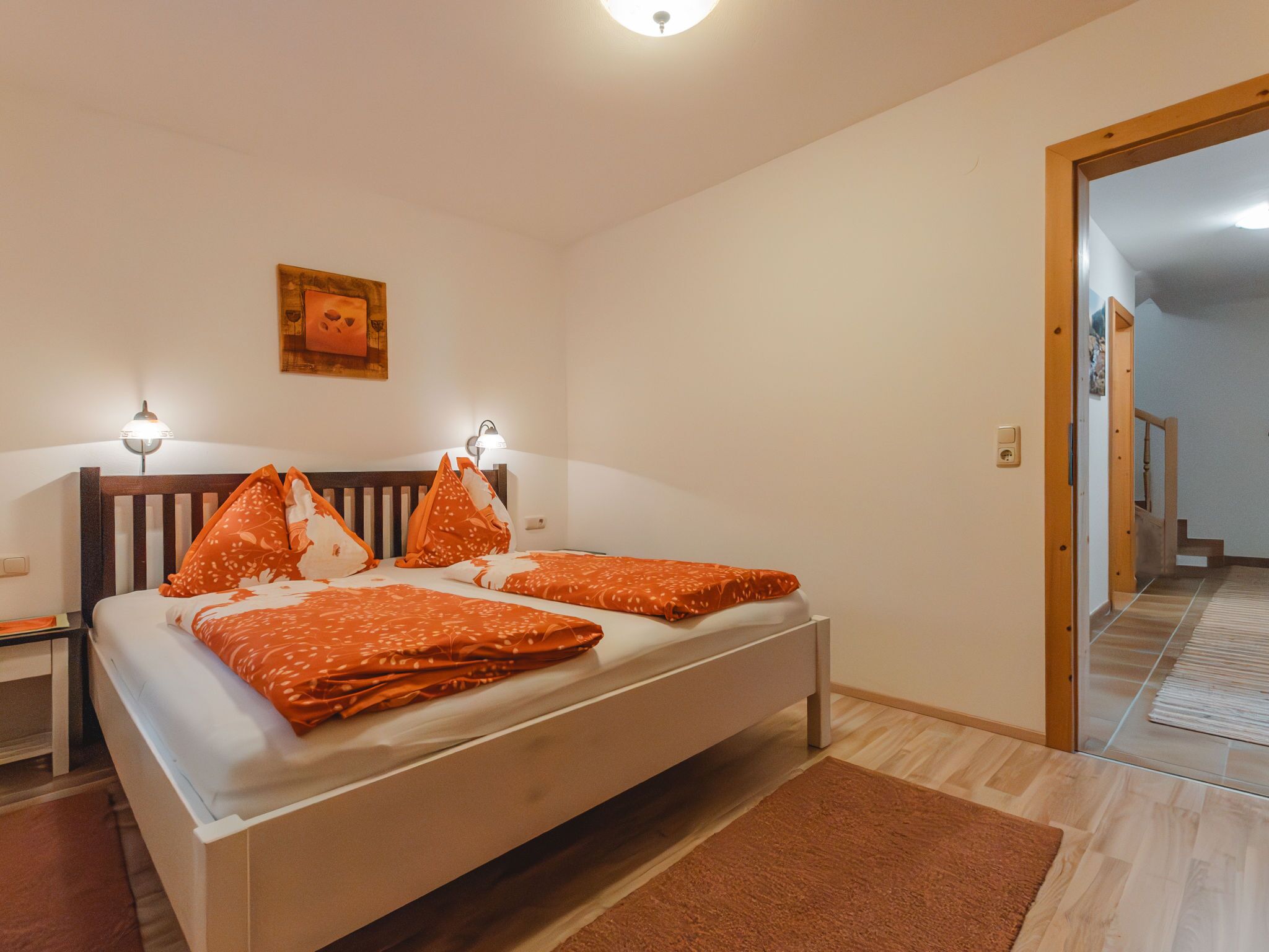 Ein Schlafzimmer mit einem Bett, zwei Nachttischlampen, einem Holz-Kopfteil, einem braunen Teppich und einer Tür zu einem anderen Raum.