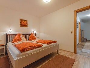 A bedroom with a bed, two bedside lamps, a wooden headboard, a brown rug, and a door leading to another room. - Ferienhaus Taubenstein by Interhome (Neukirchen am Großvenediger)
