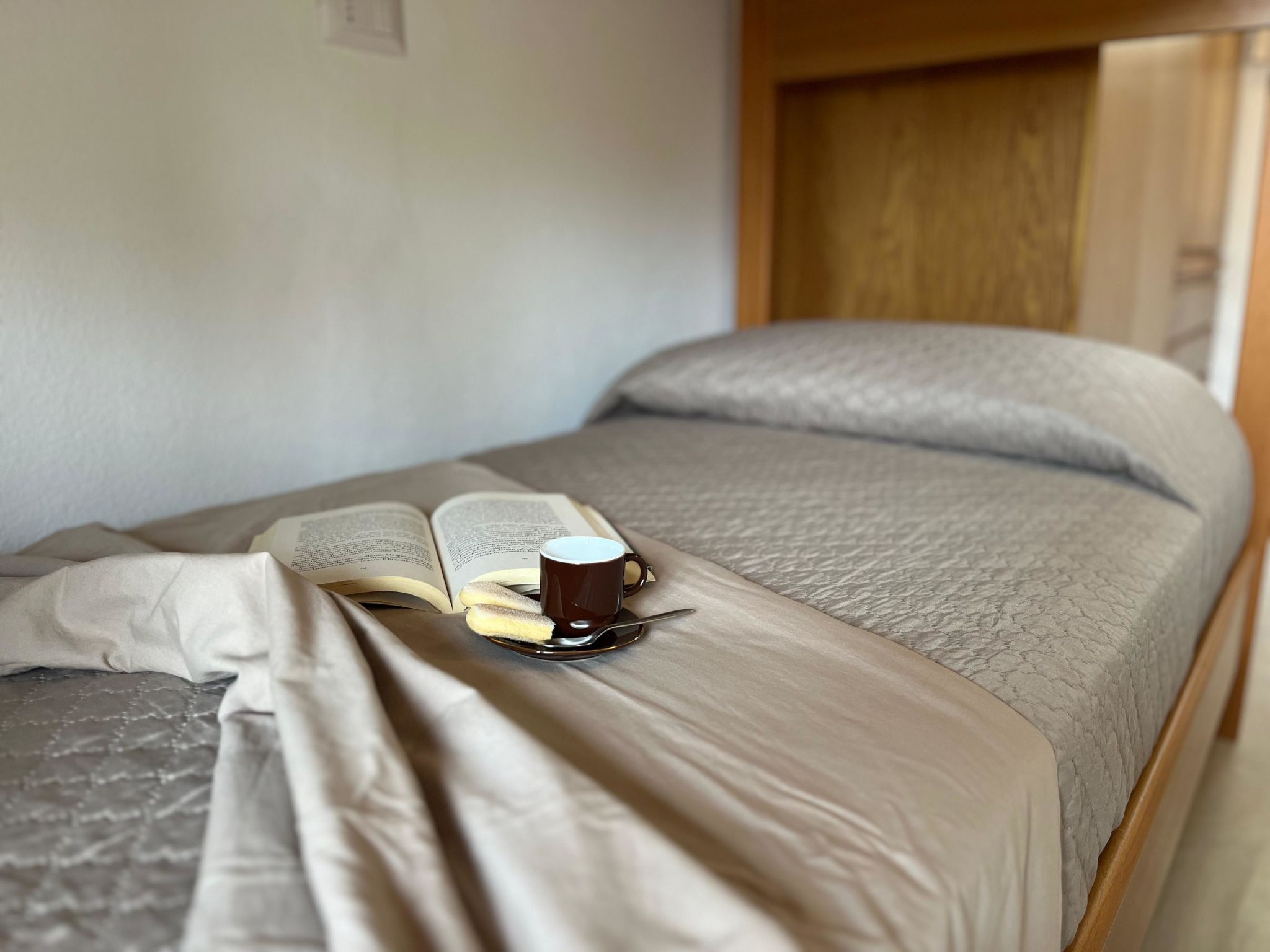 Een opgemaakt bed met een boek en een kopje erop, wat een rustige leeshoek suggereert.