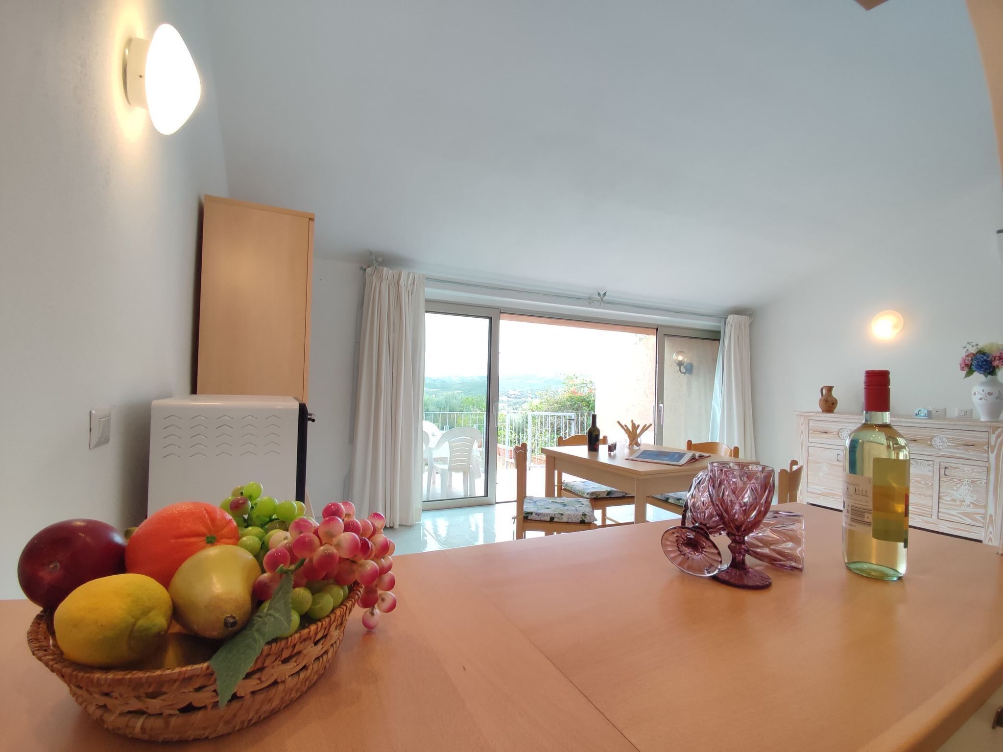 Ein Essbereich mit Tisch für zwei Personen, Obstkorb, Weinflasche und Blick ins Freie.