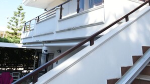 Een meerlaags gebouw met een witte gevel, een balkon met een bruin hekwerk en een trap die naar de bovenverdiepingen leidt.