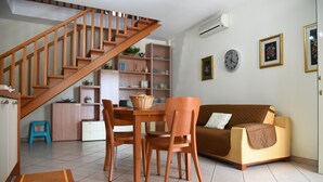 Een woonkamer met een houten trap, een bruine bank, een eettafel met stoelen en een keuken met planken.