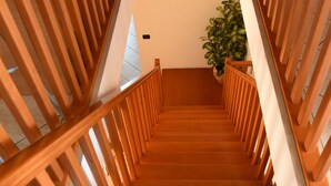 Een houten trap met een leuning, leidend naar een plateau met een bloempot.