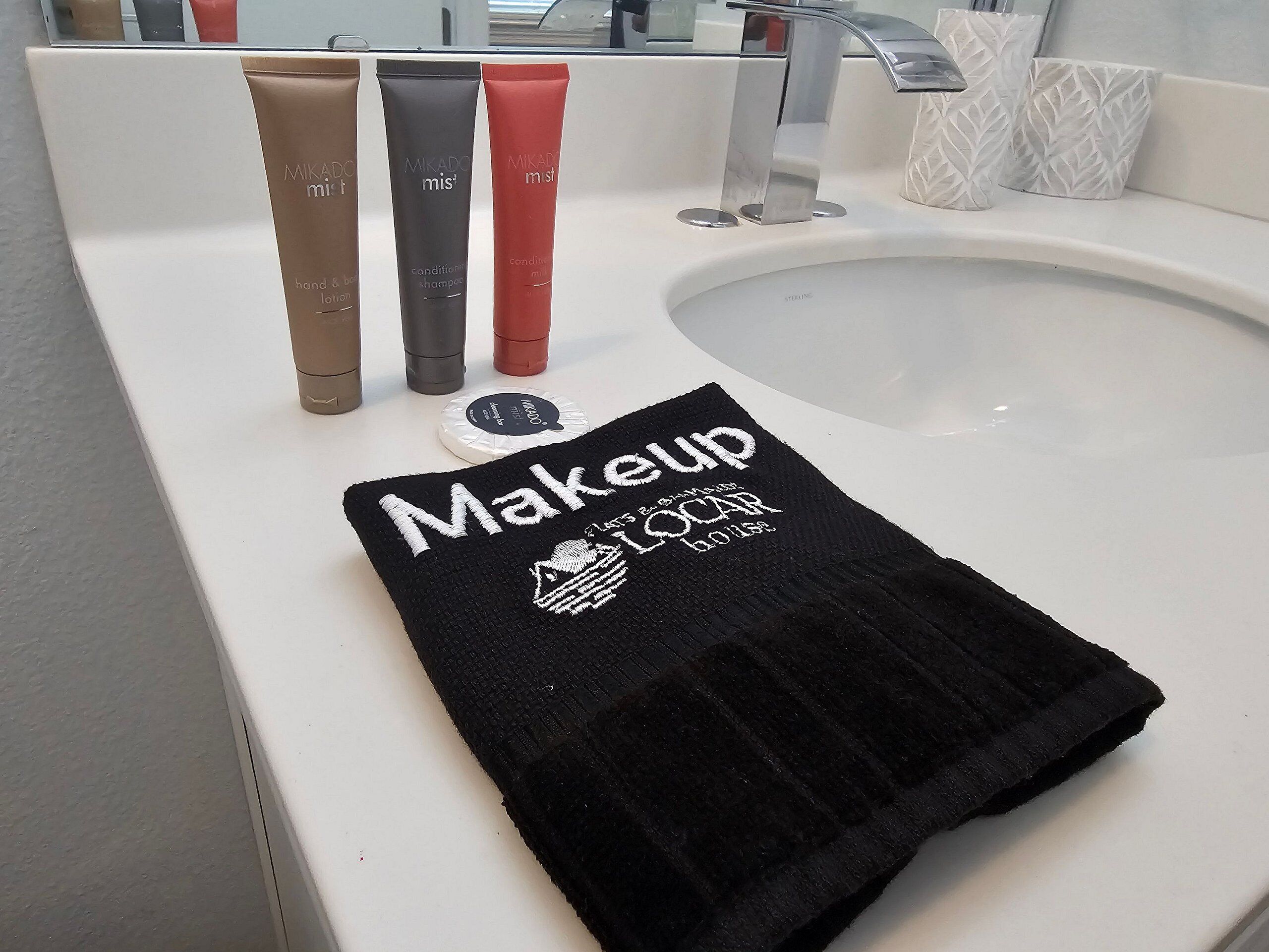 A bathroom sink with three toiletry bottles and a black towel with 'Makeup Local' text.