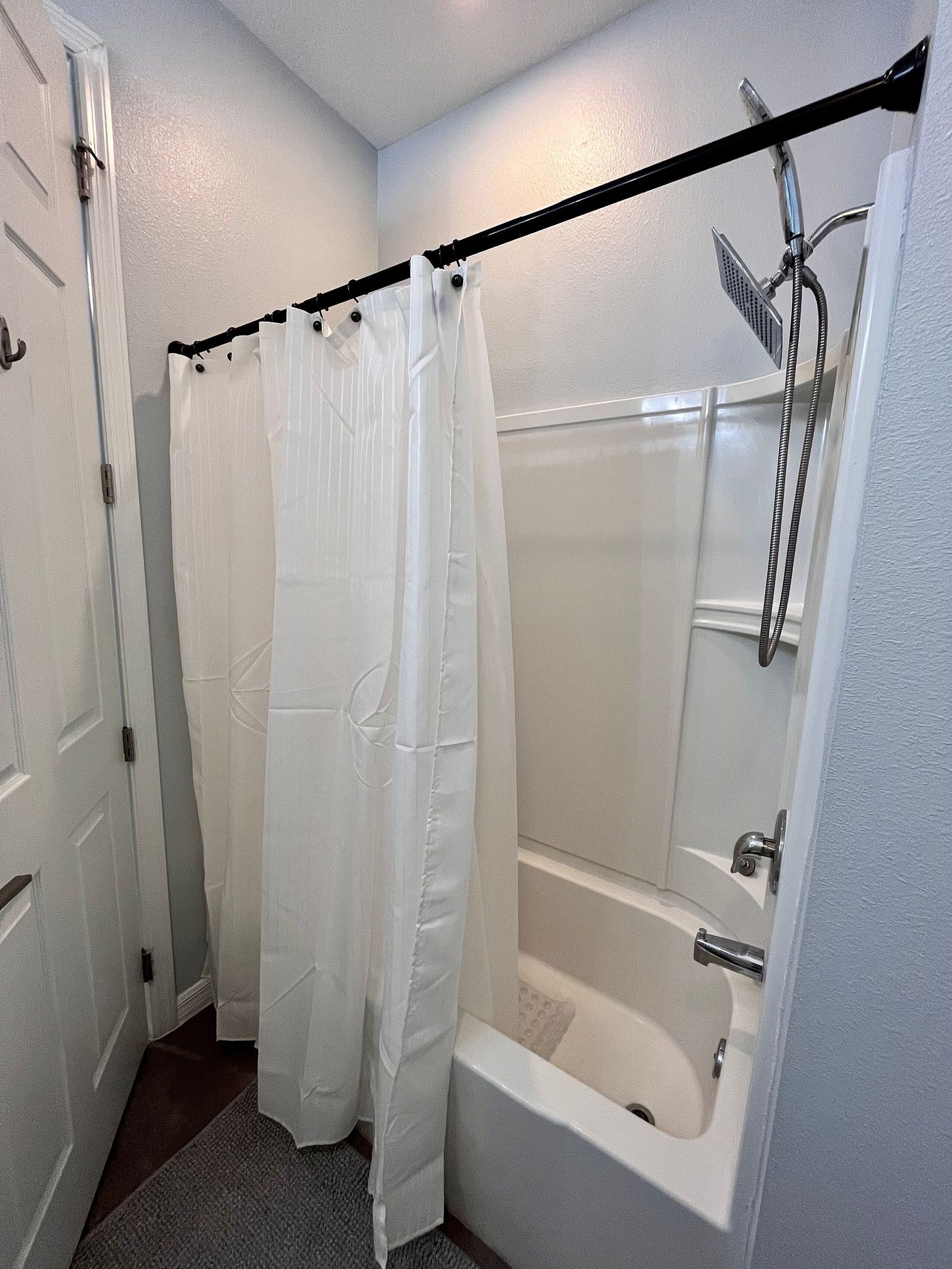 Ein Badezimmer mit Dusche, Badewanne und einer Tür mit Vorhang.