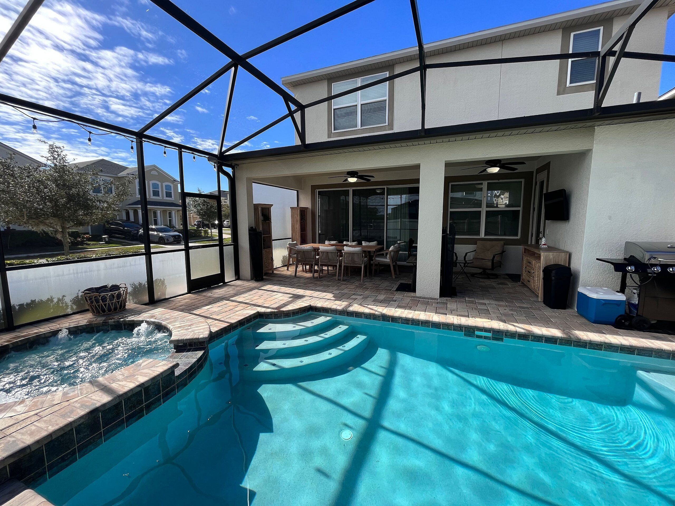 Une piscine extérieure couverte, dotée d’un patio, d’un barbecue et offrant une vue sur un quartier résidentiel.