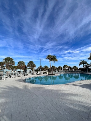 Uma área de piscina com piso de azulejos, cadeiras de descanso e guarda-sóis.