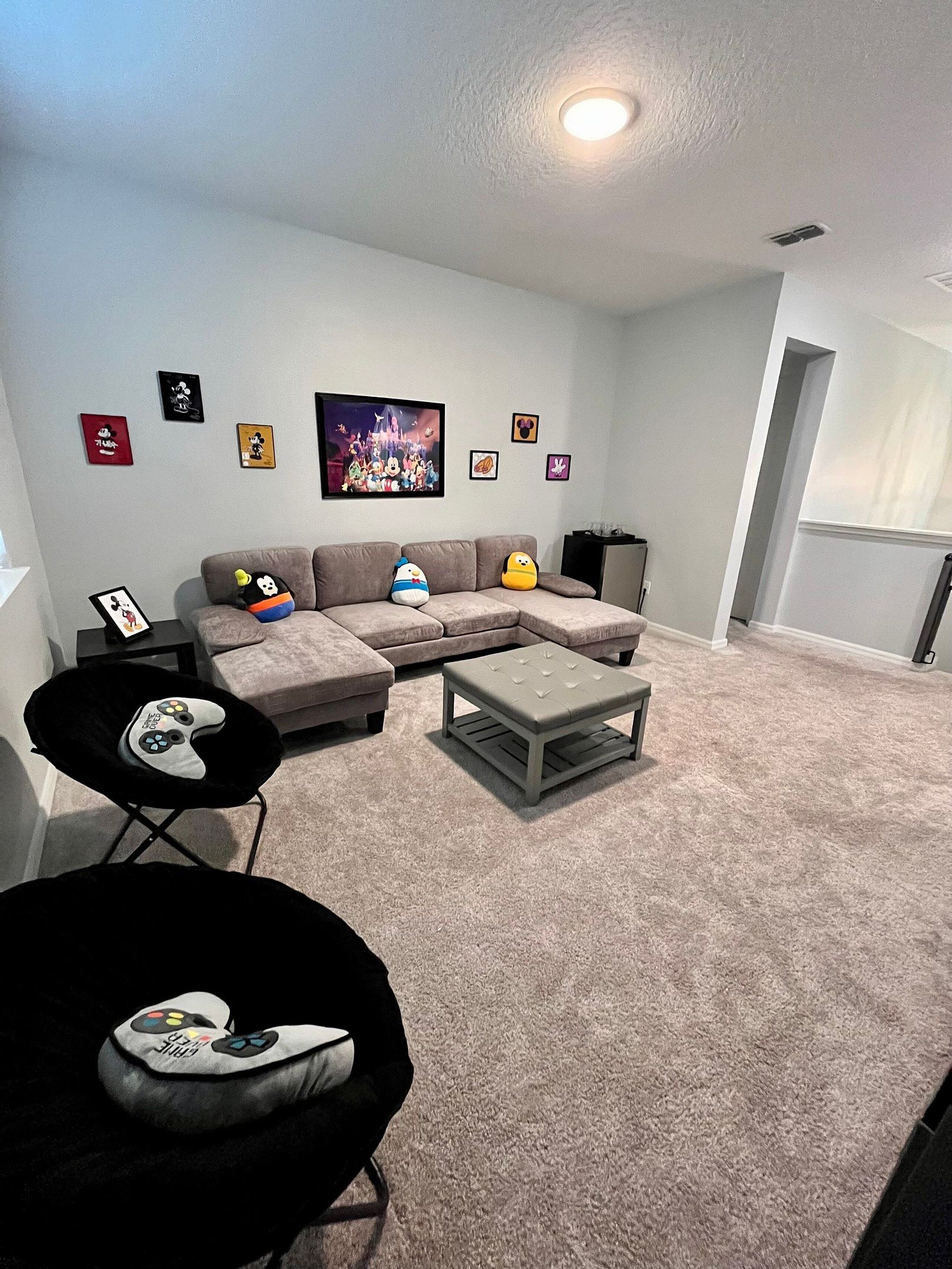 A living room with a sectional sofa, a coffee table, and a black chair with a gaming controller.