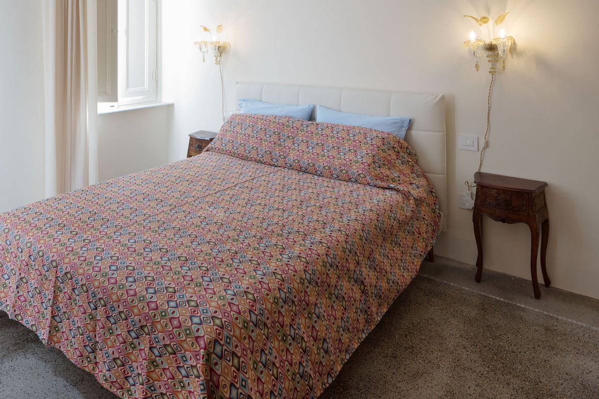 Une chambre à coucher avec un lit, un lustre, une table de chevet et une fenêtre avec des rideaux.