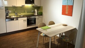 A compact kitchen with modern appliances, a dining table with chairs, and a colorful abstract painting on the wall.