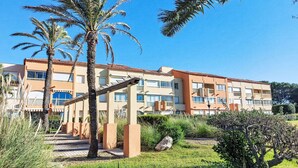 Ein mehrgeschossiges Hotel mit flachem Dach, Balkonen und einem gepflegten Garten mit Palmen und Sträuchern.