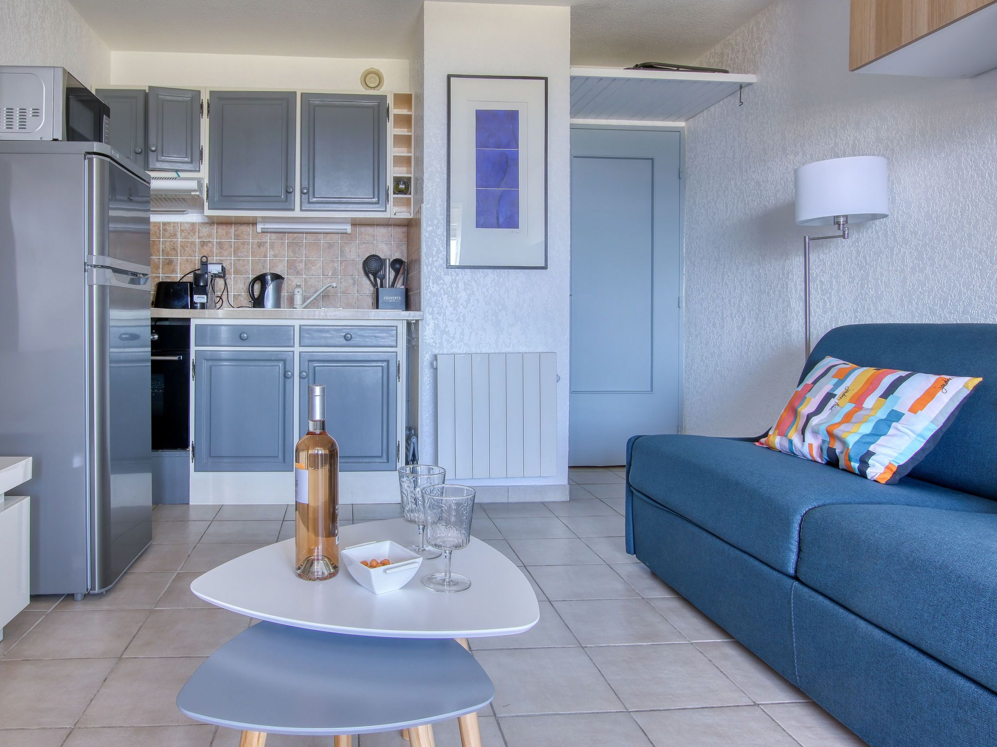 Een knus woongedeelte met een kitchenette, een eettafel, een bank en een lamp.