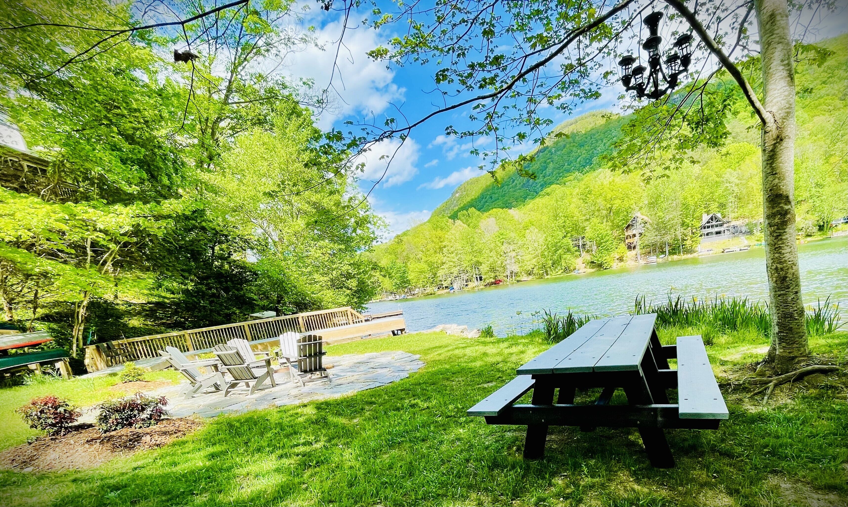 A lakeside picnic area with Adirondack chairs and a wooden deck.