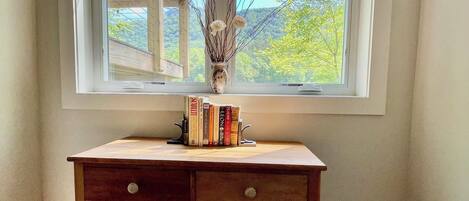 A corner room with a wooden desk, a window with a view of trees, and a vase with branches.